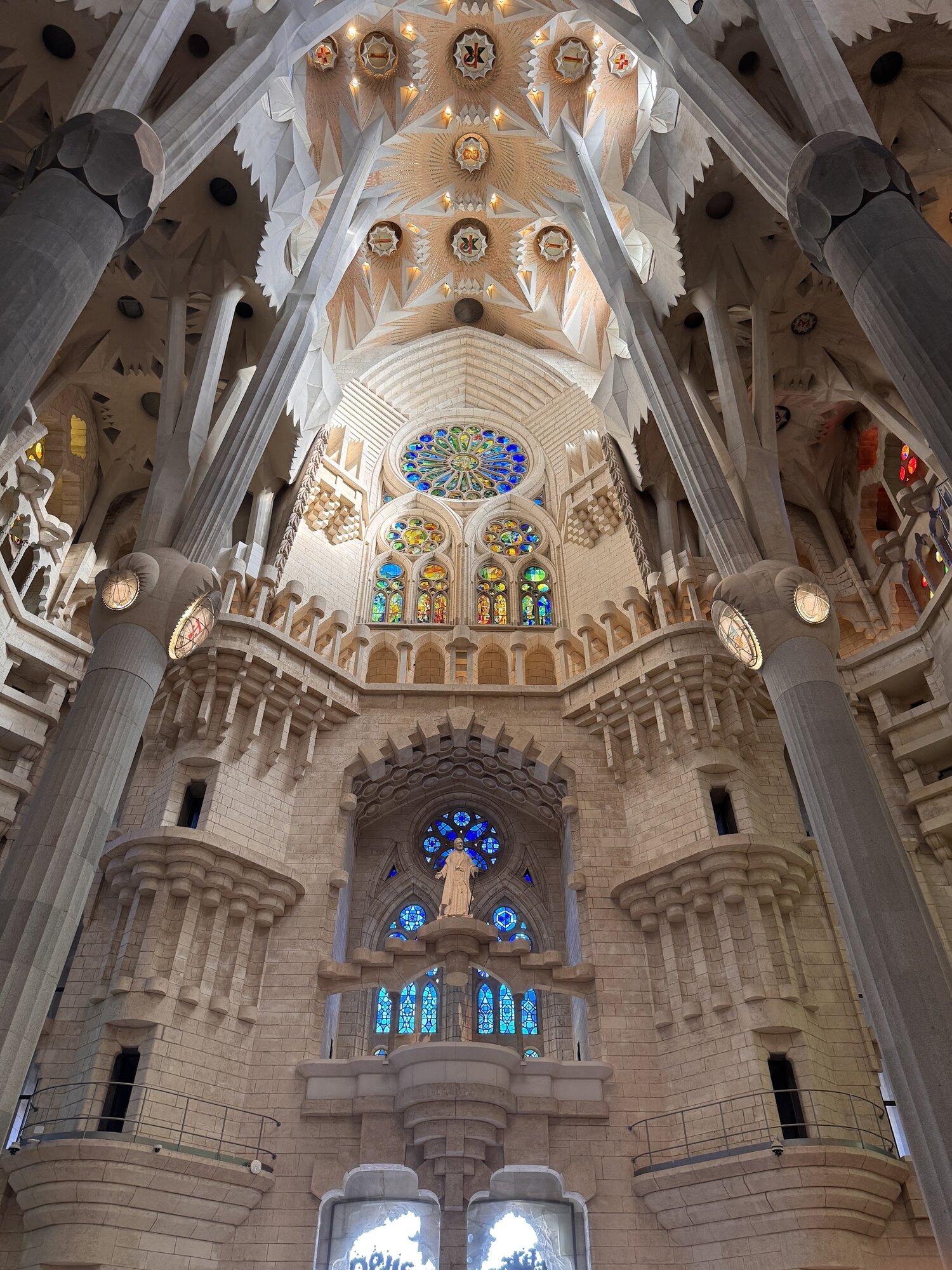 Looking up at the vaulted ceiling of the Sagrada Família, stone columns branching like trees toward a forest canopy of geometric vaults