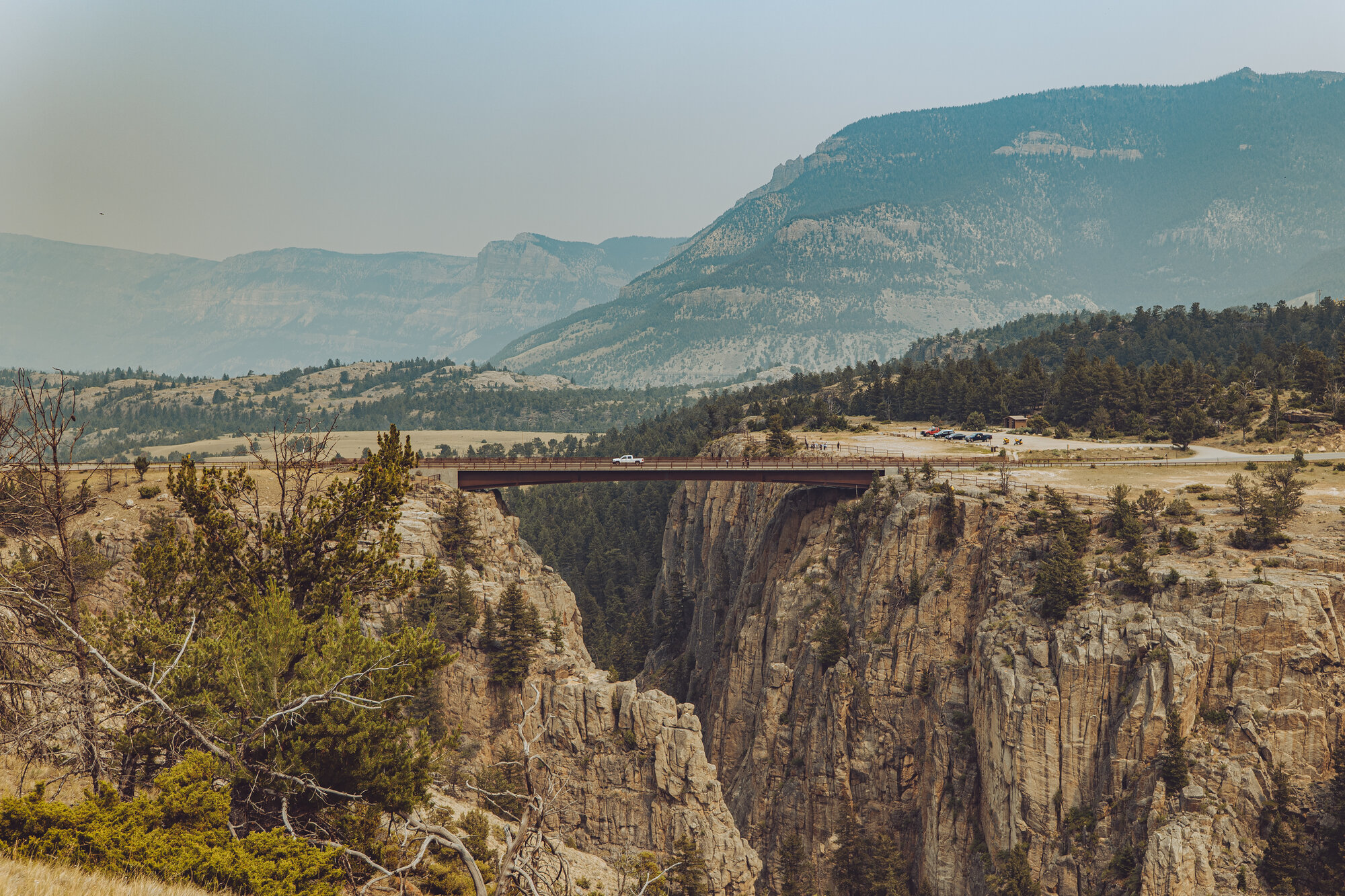 A dramatic bridge spanning a deep canyon gorge on the Chief Joseph Scenic Byway, hazy mountains and forested hills beyond