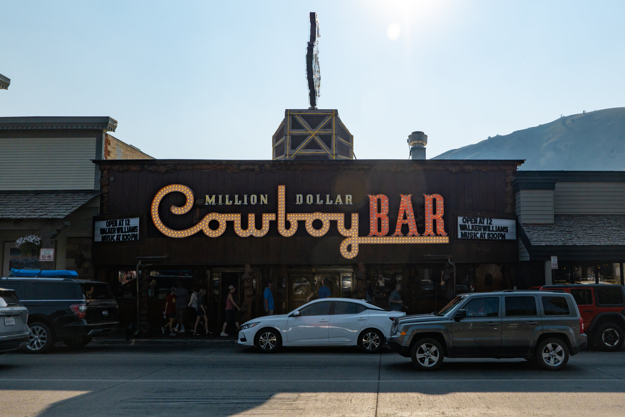The Million Dollar Cowboy Bar facade in Jackson, Wyoming, with its famous neon sign lit up in the afternoon sun