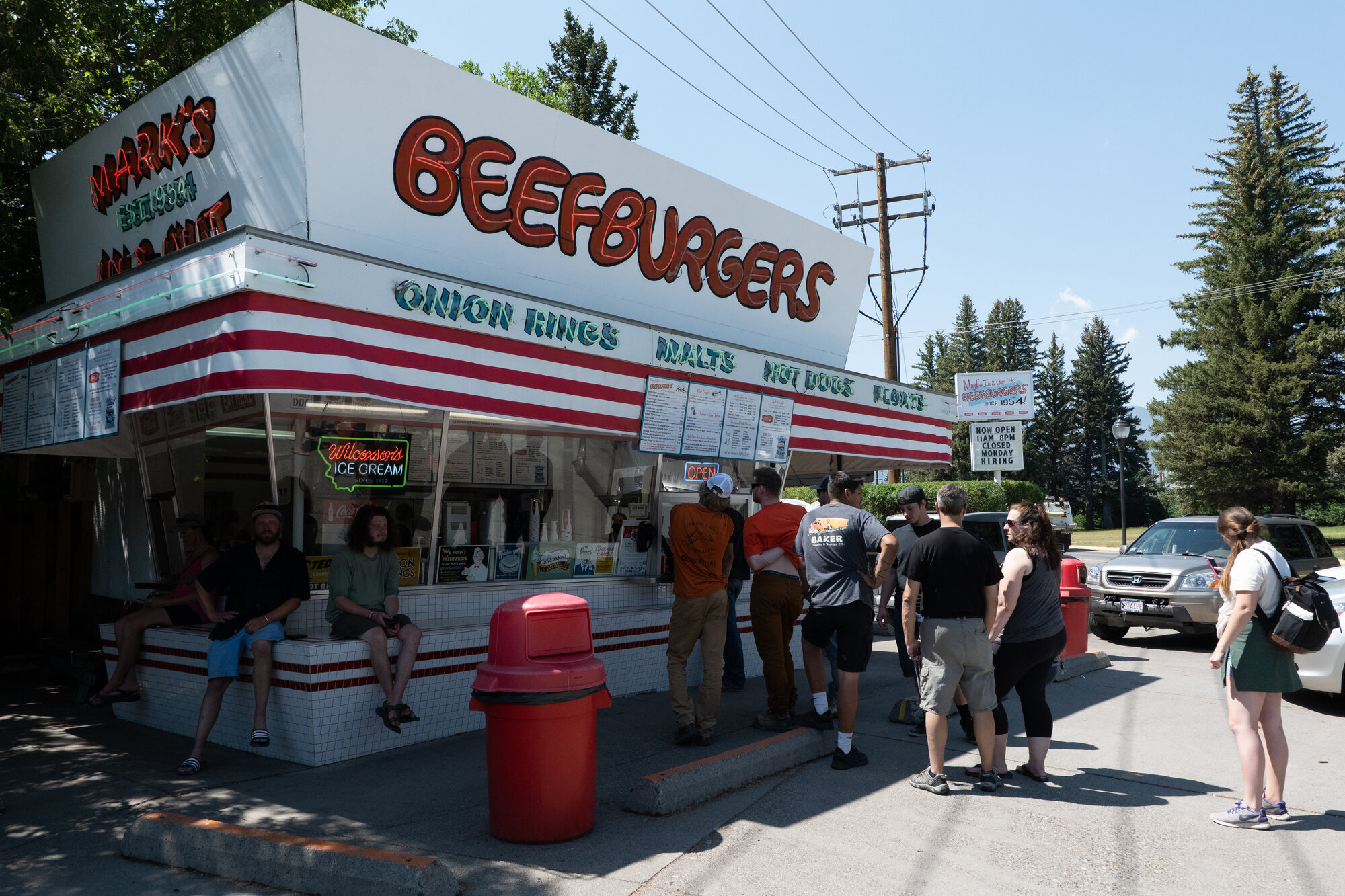 Mark's In and Out burger stand in Bozeman, Montana with a line of customers out front under a bright summer sky