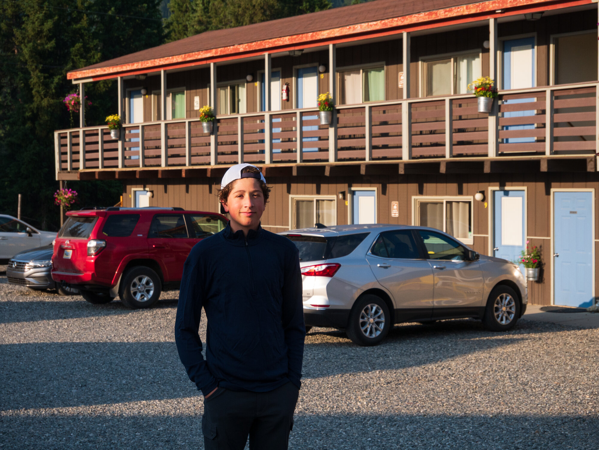 Niko standing in the parking lot outside the High Country Cabins in Cooke City at dusk, casual and relaxed before the hike begins