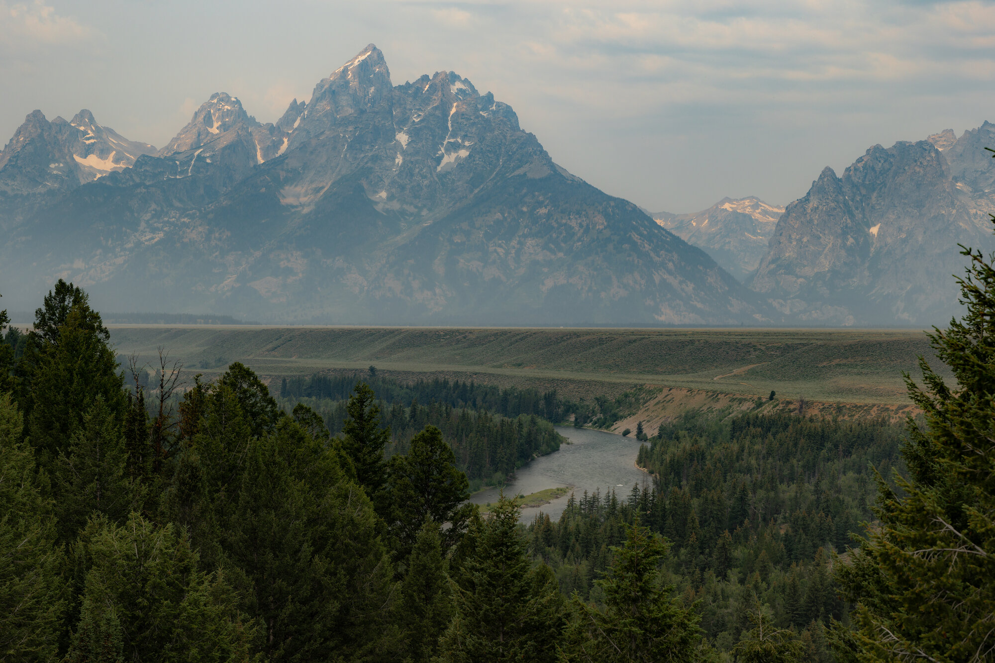The Snake River Overlook in Grand Teton National Park, the river winding through a forested plain with the Teton Range rising through wildfire haze behind
