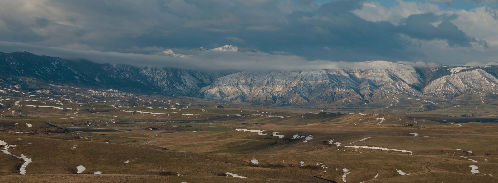 The Bighorn Mountains rising above patchy snow and golden winter grasslands under a dramatic overcast sky in northern Wyoming