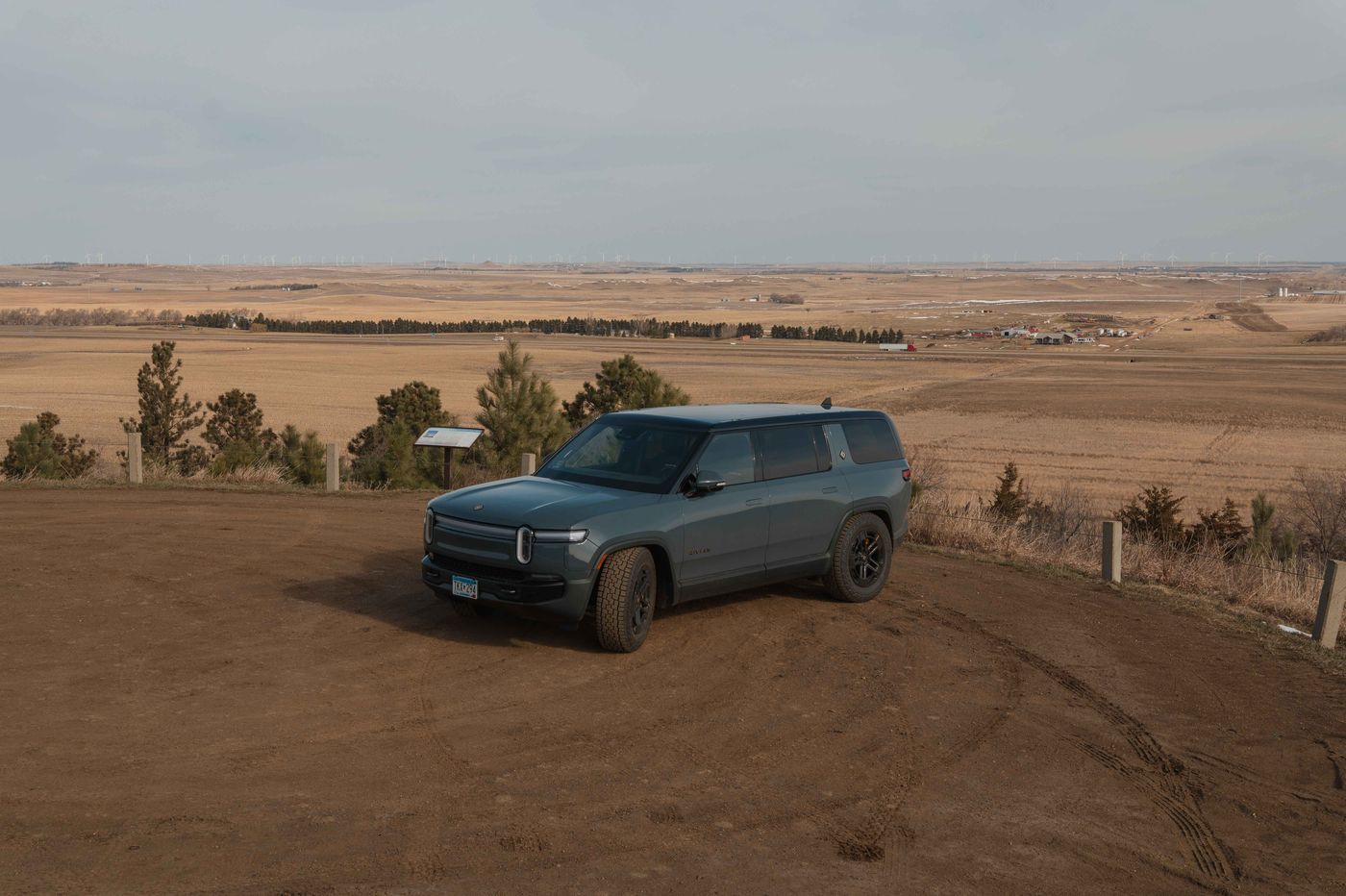 A dark Rivian SUV parked on a dirt pullout at the Salem Sue fiberglass cow parking lot